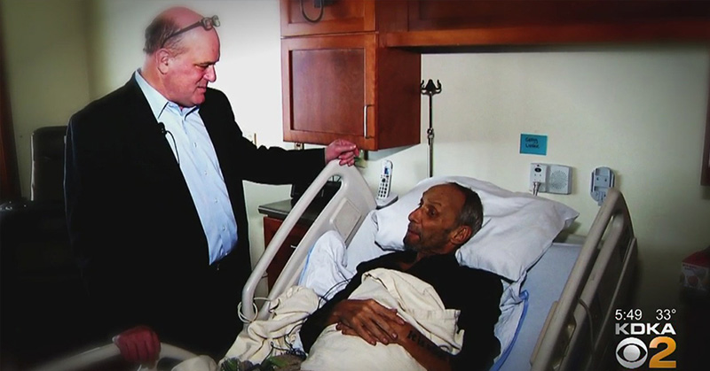 A man visiting another person laying in a hospital bed