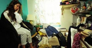 woman sitting in messy room surrounded by clutter
