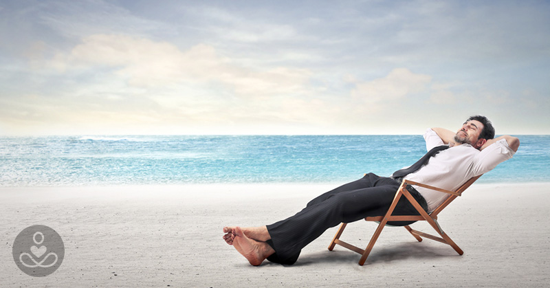 Man in a button up shirt, tie and slacks reclining in a chair on the beach