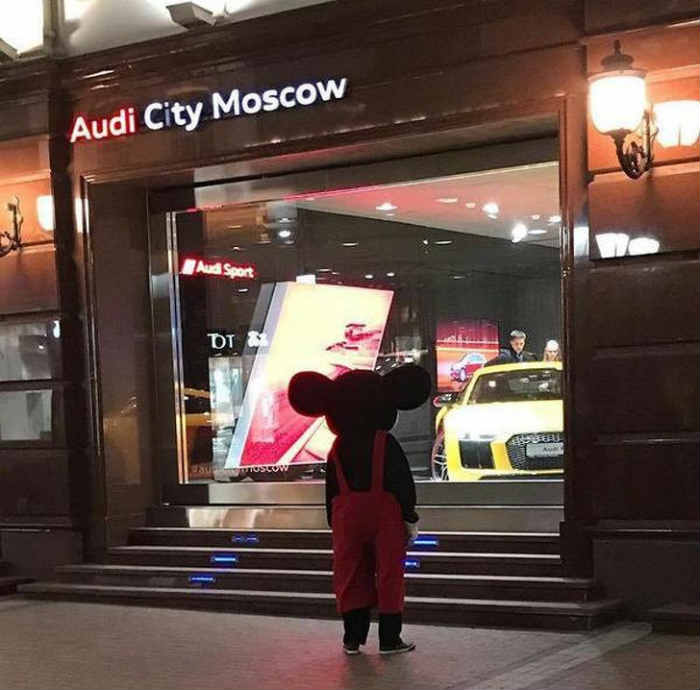 A man wearing a Mickey Mouse costume stopped to look at expensive cars.
