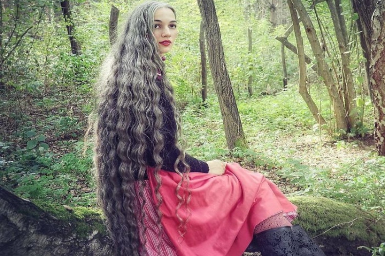 Woman in a red dress and black sweater with very long grey hair