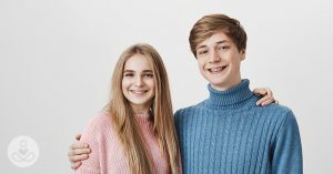 Having a Sister Is Beneficial To Your Mental Health, Studies Show girl in pink sweater hugging her brother in a blue ribbed turtleneck