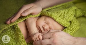 Here’s Why We Should Ditch Throwing New Moms Baby Showers For Postpartum Parties baby wrapped in a lime green blanket