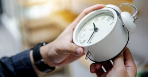 Changing our clocks is a health hazard. Just ask a sleep doctor person holding white alarm clock