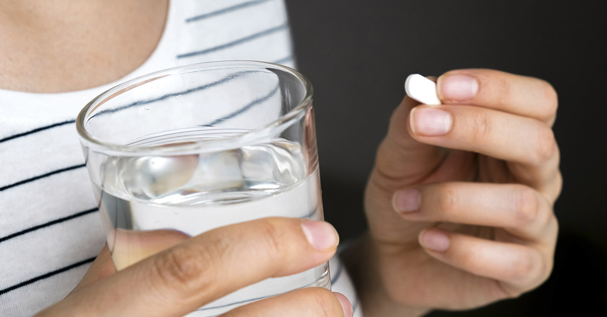 person holding glass of water and medication
