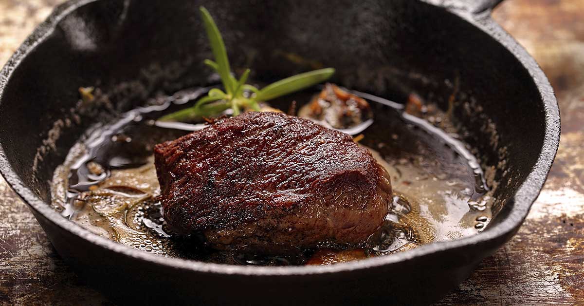 cast iron pan containing a sizzling steak