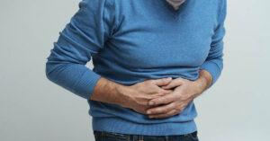 Surprising Crohn’s Symptoms You Should Know man in blue sweater holding abdomen