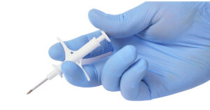World’s Smallest Implantable Chip Can Monitor Medical Conditions hand with blue latex glove holding a small injection device