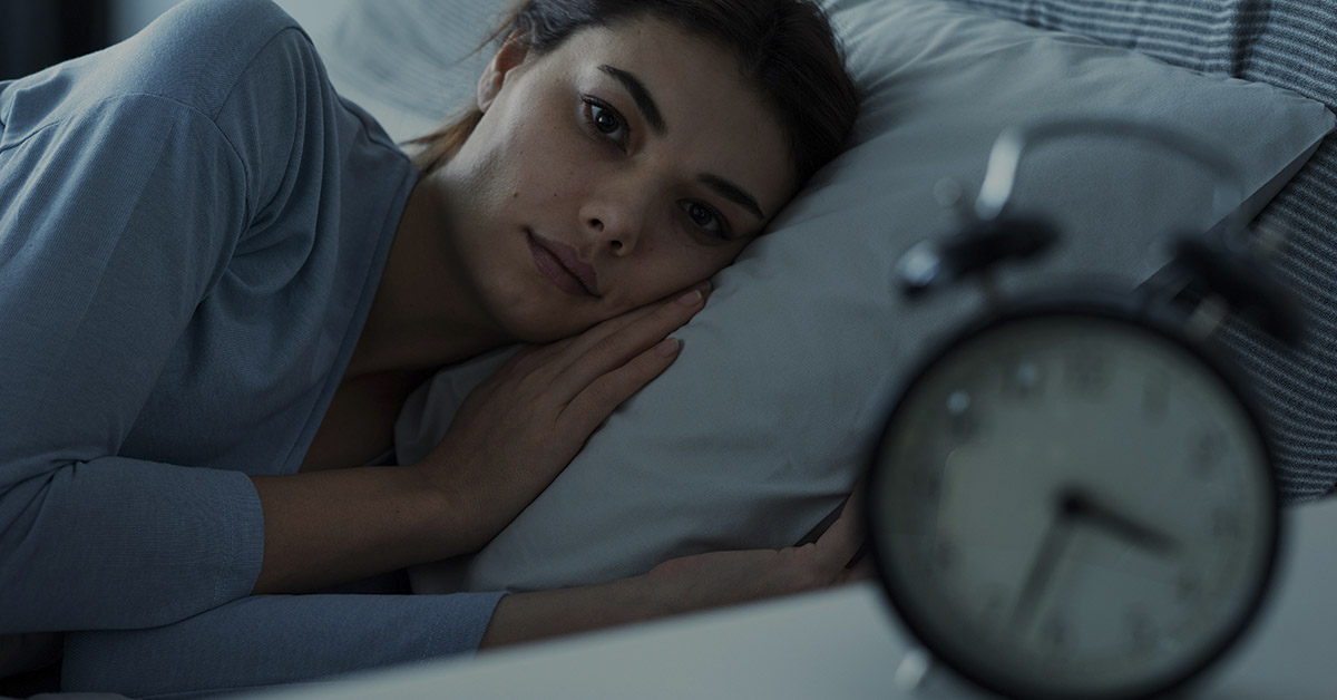 woman in bed staring at alarm clock