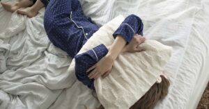 The 10 Best Natural Hangover Cures person laying in bed with pillow over face due to hangover