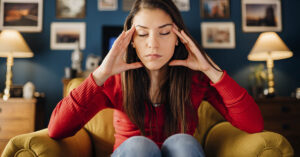 woman sitting with hands placed on each side of face, eyes closed, concentrating