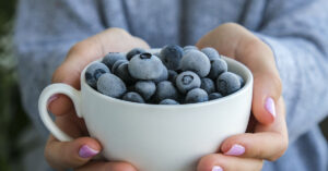 Woman holding bowl with Frozen blueberry fruits. Harvesting concept. Female hands collecting berries.