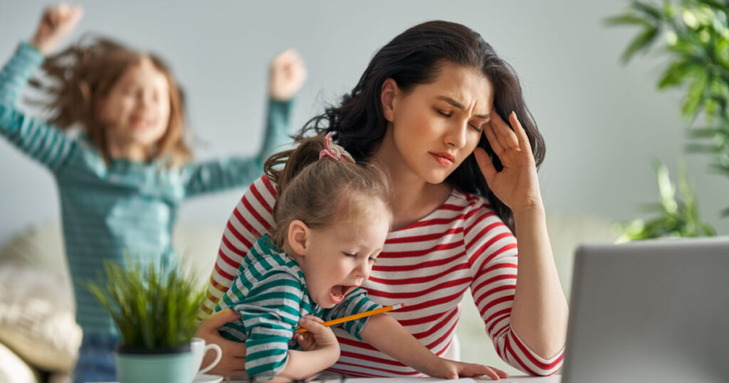 Stressed mother of two working at computer holding screaming toddler