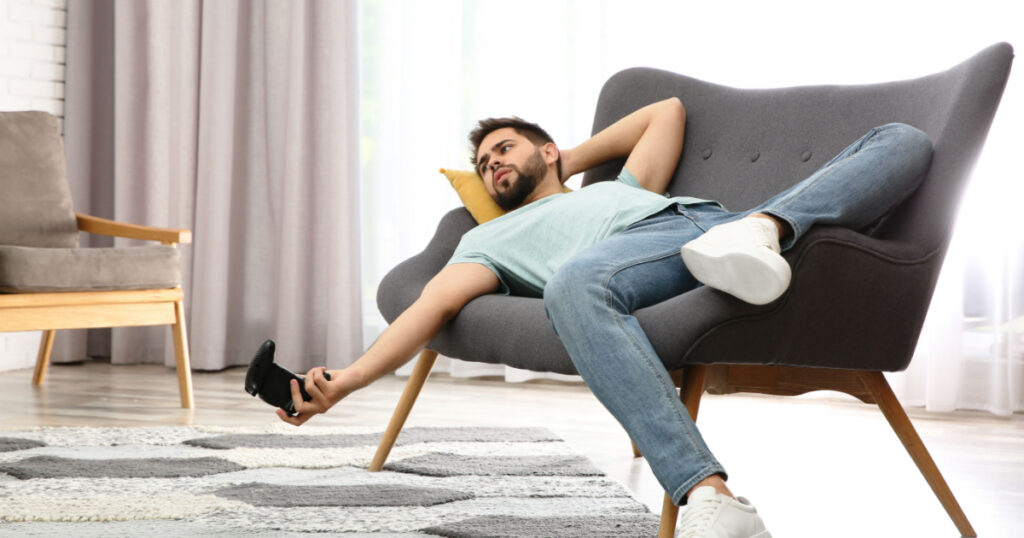 Lazy young man playing video game while lying on sofa at home