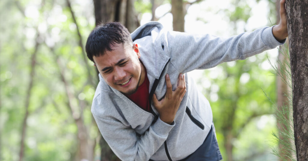 man holding chest in pain while in the woods