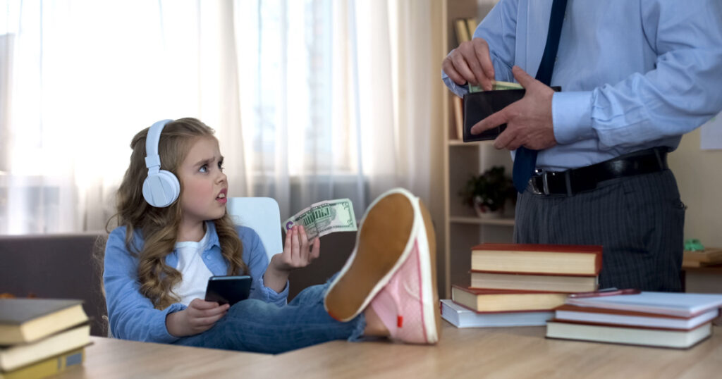 Busy father giving pocket money to little capricious daughter with headphones