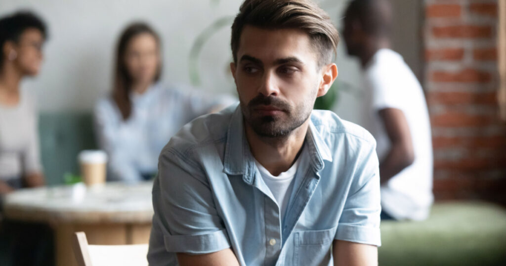 guy sitting apart, separately of others teenagers feels unhappy having problems with communication

