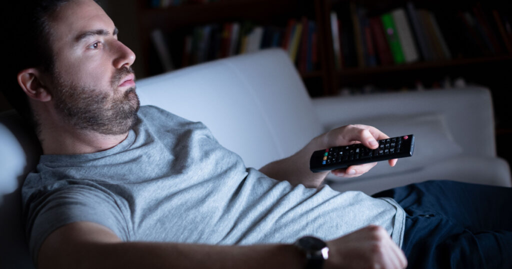 Lazy man watching television at night alone