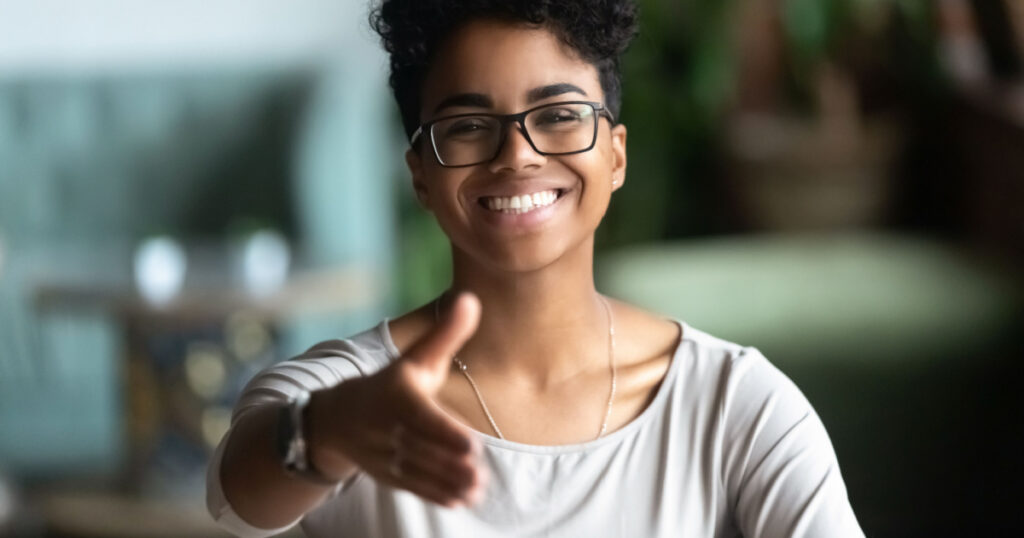 Happy african American young woman in glasses stretch hand for handshake greeting introducing to someone, smiling black biracial millennial female hr agent in spectacles get acquainted at meeting