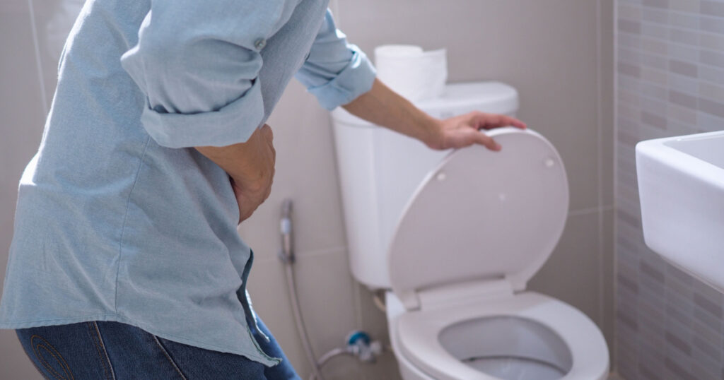 Hombre agarrando el estómago levantando la tapa del inodoro en el baño