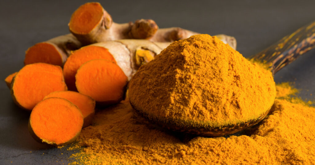 Turmeric (curcumin) powder in a wooden ladle and fresh rhizome on a black background,For spices and medicine.

