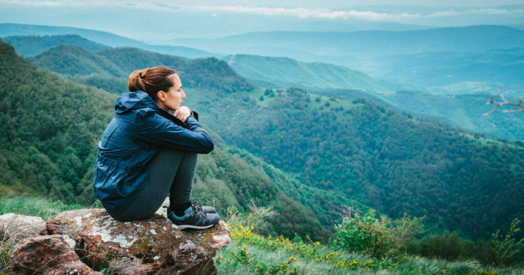 Sad depressed woman adult sitting on mountain rock worried anxious thinking of problems on mountain view in nature