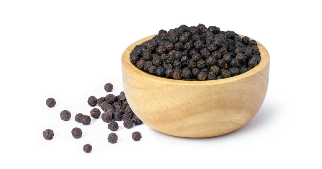 black pepper seeds or peppercorns (dried seeds of piper nigrum) in wooden bowl