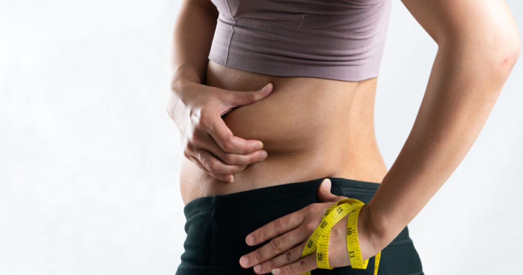 woman hand pinching on her excessive belly fat waist with measure tape