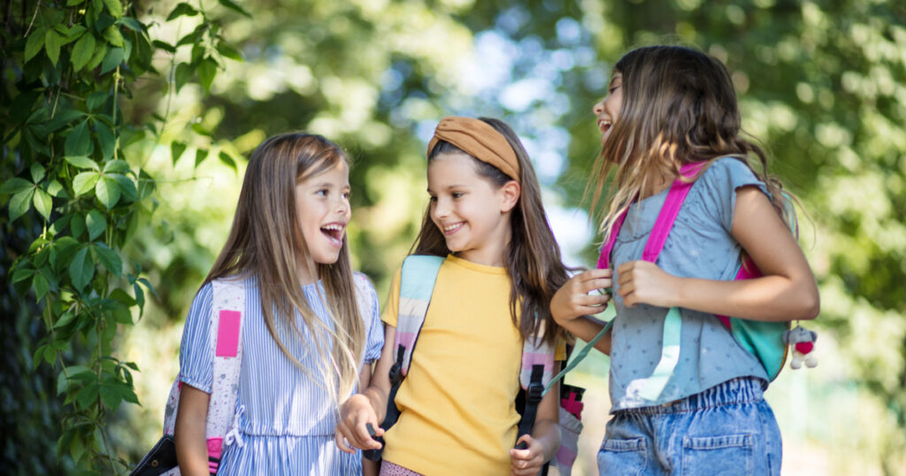 Three smiling little girls carrying school and and going to school 