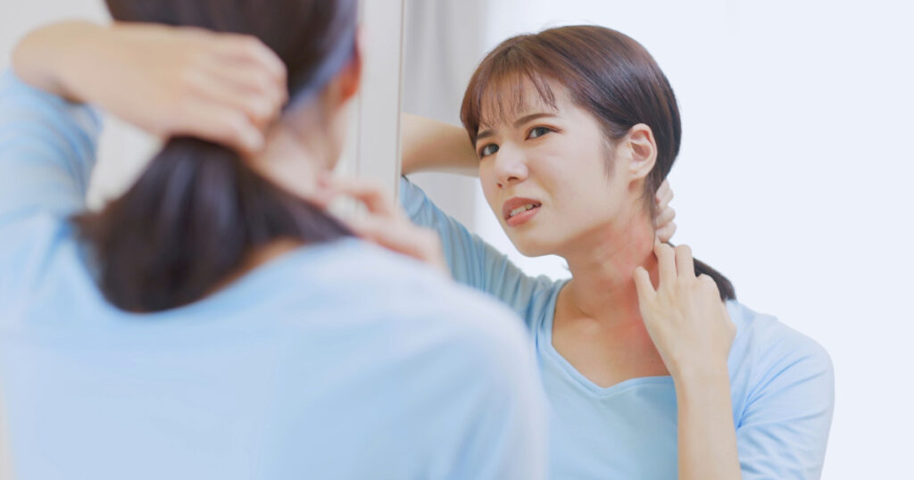 Primer plano de una mujer asiática que tiene la piel seca y se rasca el cuello frente al espejo en casa