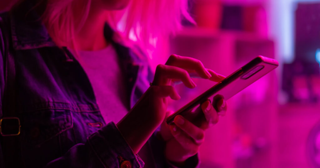 Close-up of a young blonde woman with a mobile phone in her hands in the pink neon light
