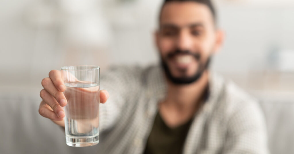 man showing glass of fresh clear water at camera