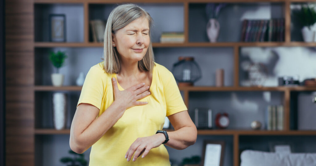 Older woman at home doing fitness has severe shortness of breath and chest pain, compares bullets on fitness bracelets