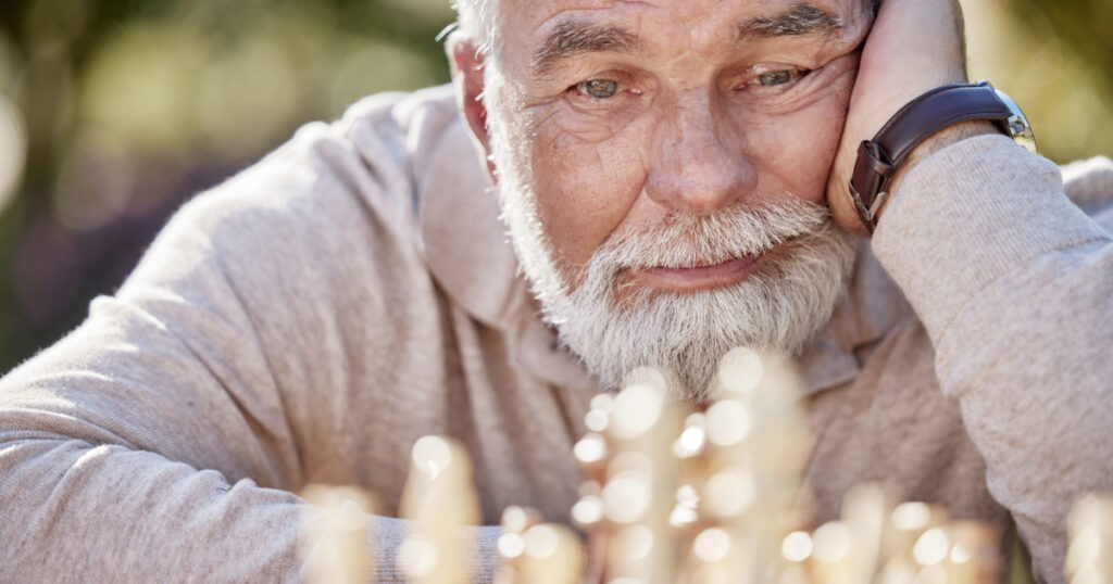 senior man playing a game of chess outside and looking unhappy