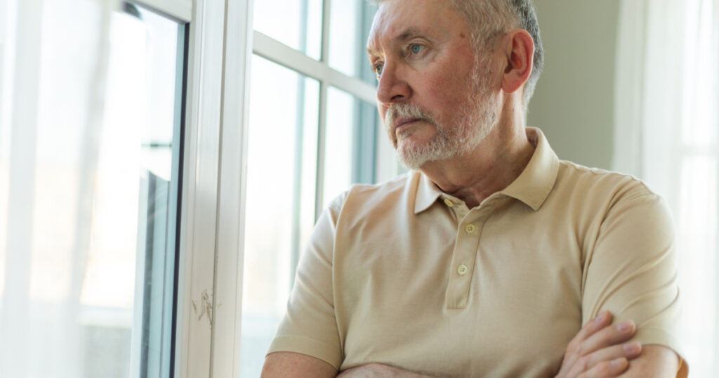 Unhappy grandfather looking sadly outside window