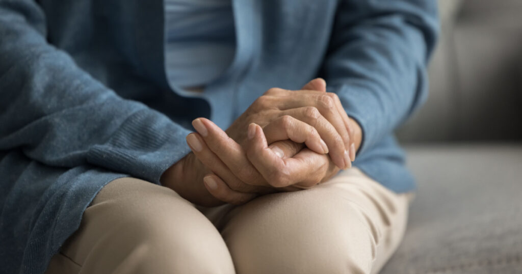 Mature old woman holding hands, folded palms on lap