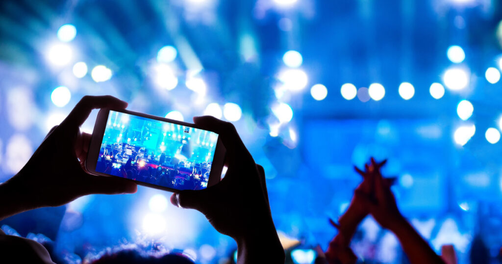 person taking photos with phone at concert