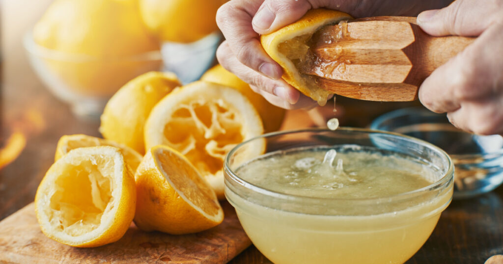 squeezing fresh lemon juice with wooden reamer into bowl