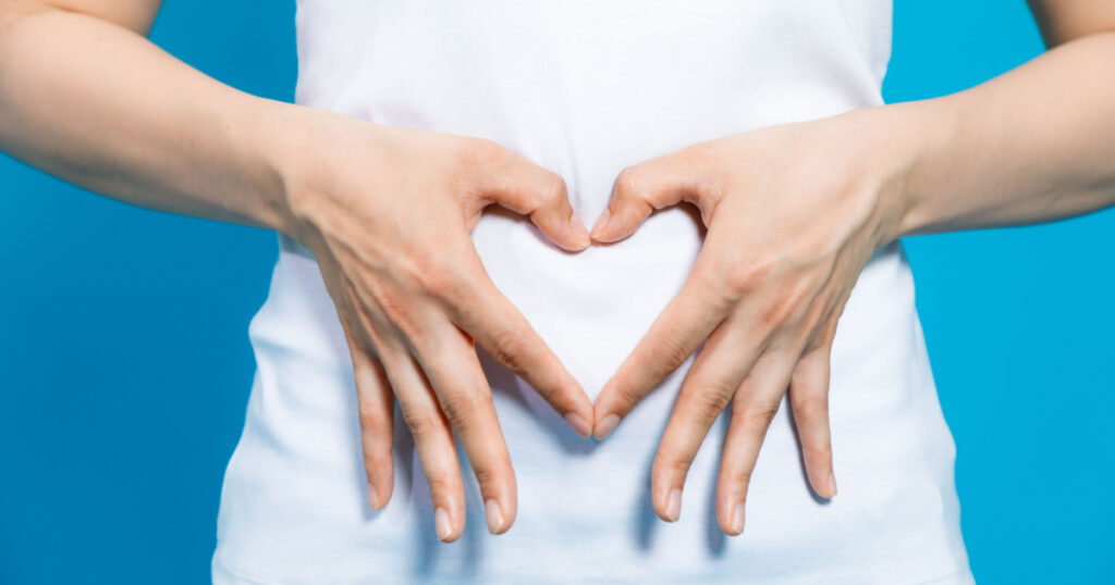 young woman who makes a heart shape by hands on her stomach.