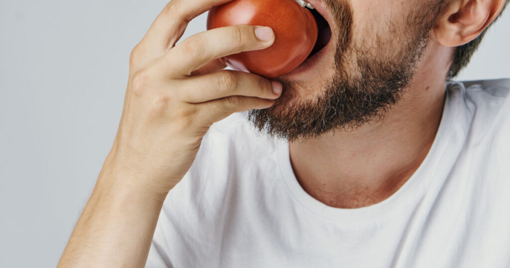 man eats a tomato