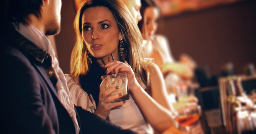 Young woman with a glass of wine talking to a man at the bar
