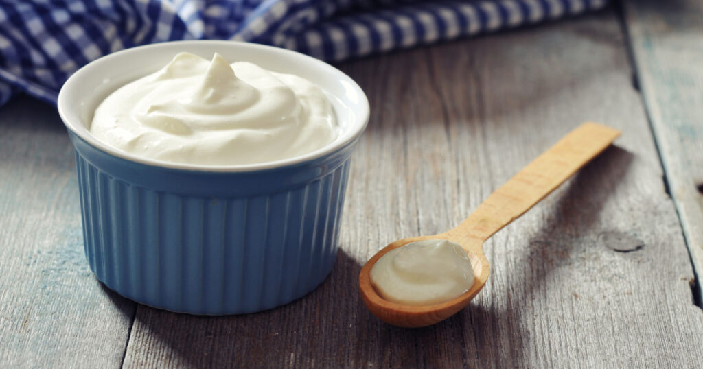 Greek yogurt in a ceramic bowl with spoons on wooden background