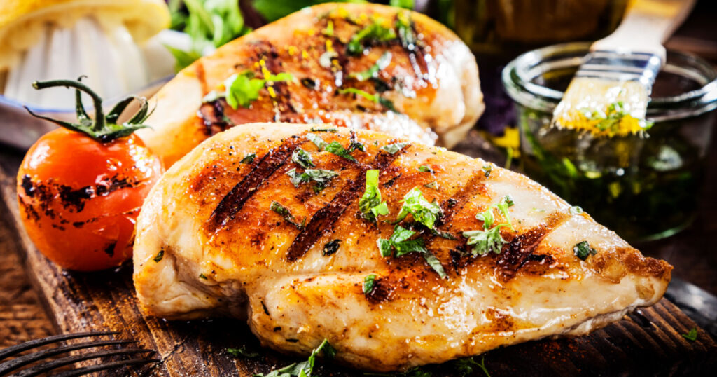 Marinated grilled healthy chicken breasts cooked on a summer BBQ and served with fresh herbs and lemon juice on a wooden board, close up view