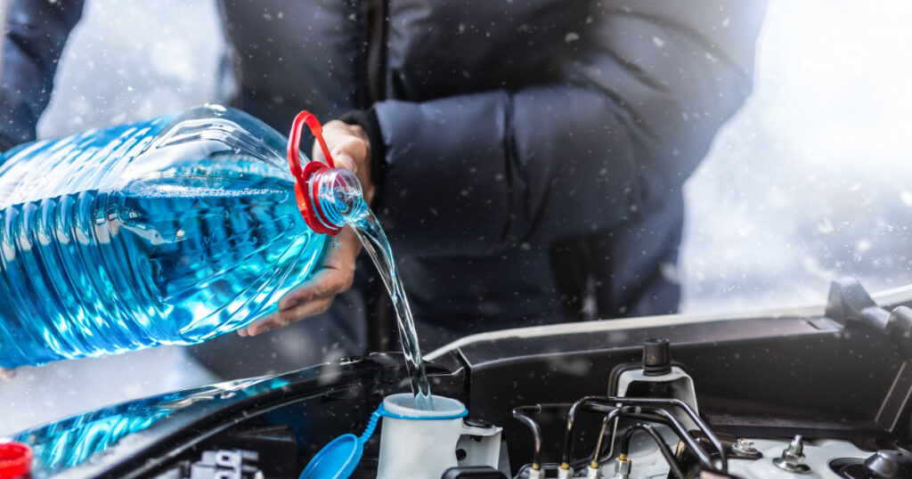 The male driver pours antifreeze into the tank to spray the windshield during a snowstorm.
