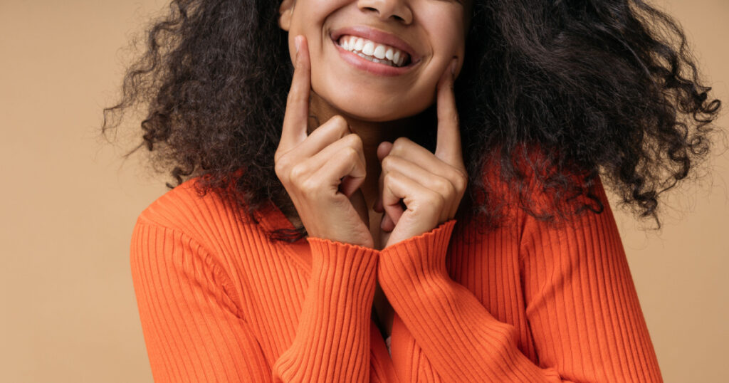 Close up portrait of young happy African American woman pointing pinger on white teeth isolated on background. Health care, dental treatment, oral hygiene concept
