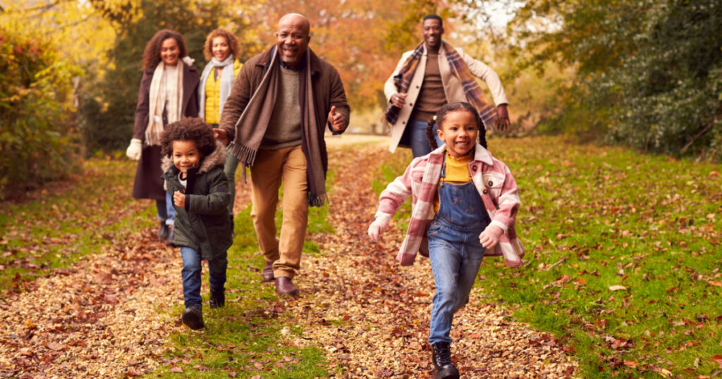 Smiling Multi-Generation Family Having Fun With Children Walking Through Autumn Countryside Together
