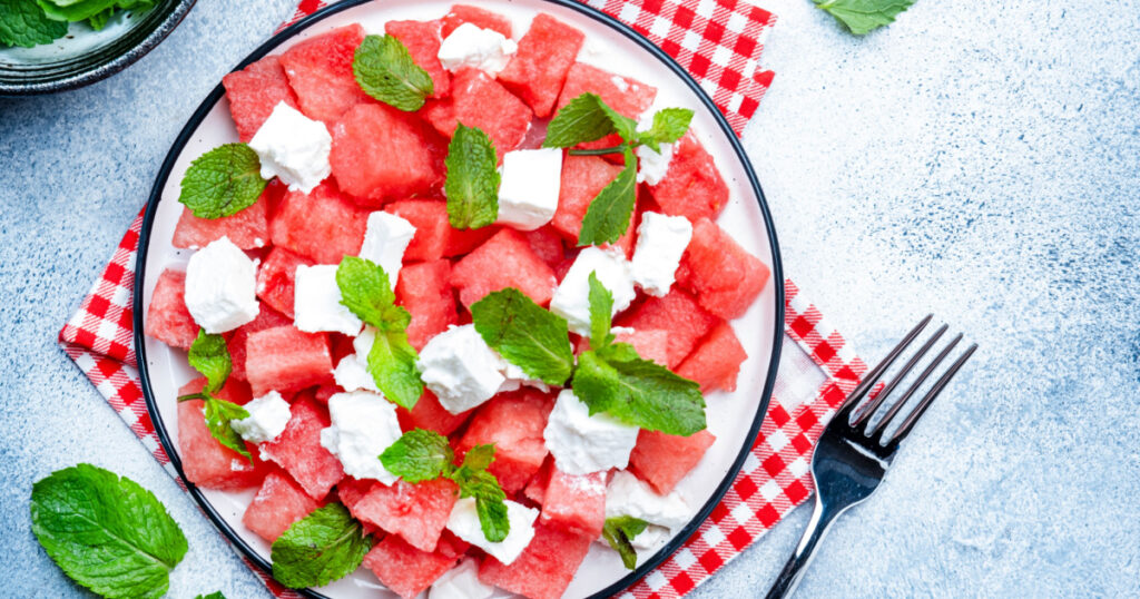 Refreshing summer juicy Watermelon salad with feta cheese and fresh mint, gray table background, top view, copy space
