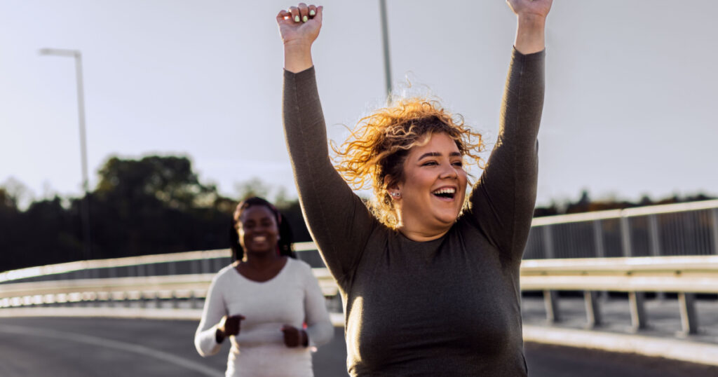 Two excited young plus size women jogging together.
