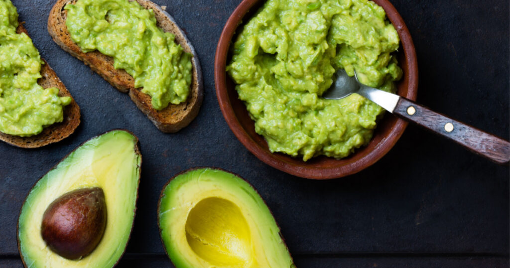 Traditional latinamerican mexican sauce guacamole in clay bowl, cut half avocado and avocado sandwiches on dark background weight loss foods Top view
