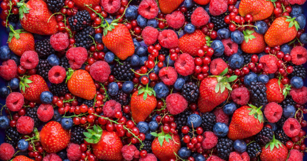 Berries overhead closeup colorful assorted mix of strawberry, blueberry, raspberry, blackberry, red currant in studio on dark background
